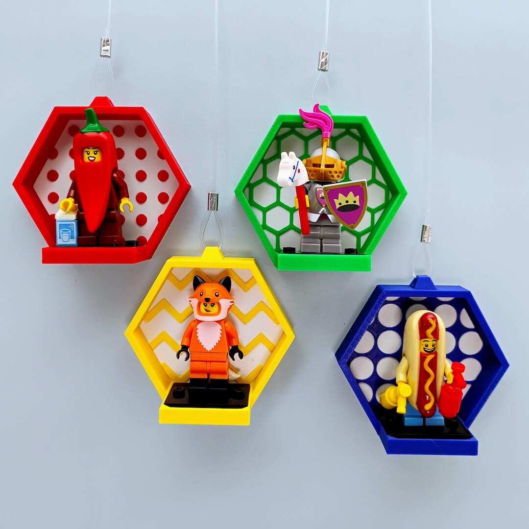 Hanging LEGO® minifigure displays on a sunny window using clear suction hooks, hexagon frames in assorted colors with studs, hexagons, zig-zags, and circles patterns
